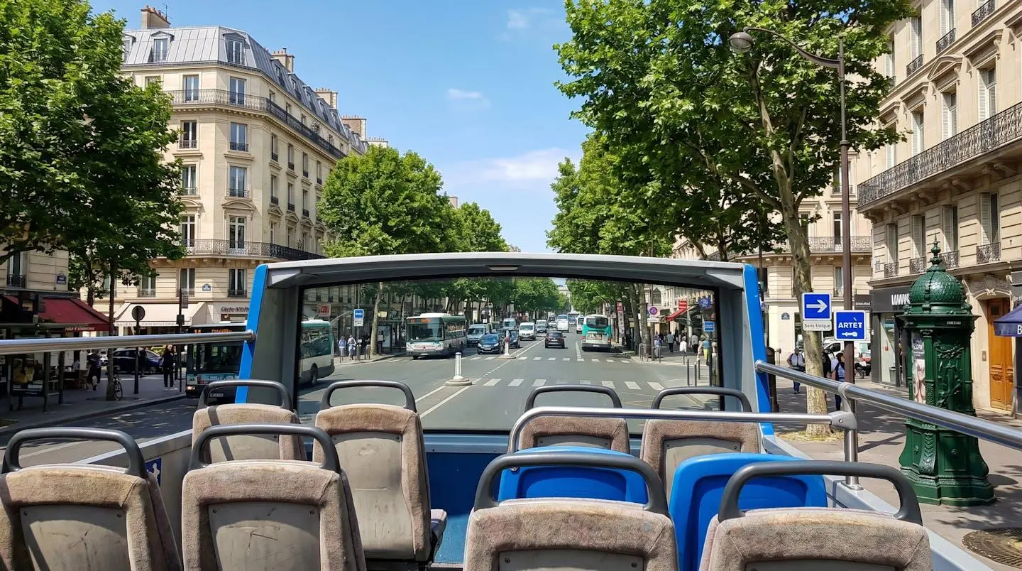 Wide-angle view from an open-top bus upper deck showing classic Parisian Haussmanian architecture and tree-lined boulevard on a bright sunny day